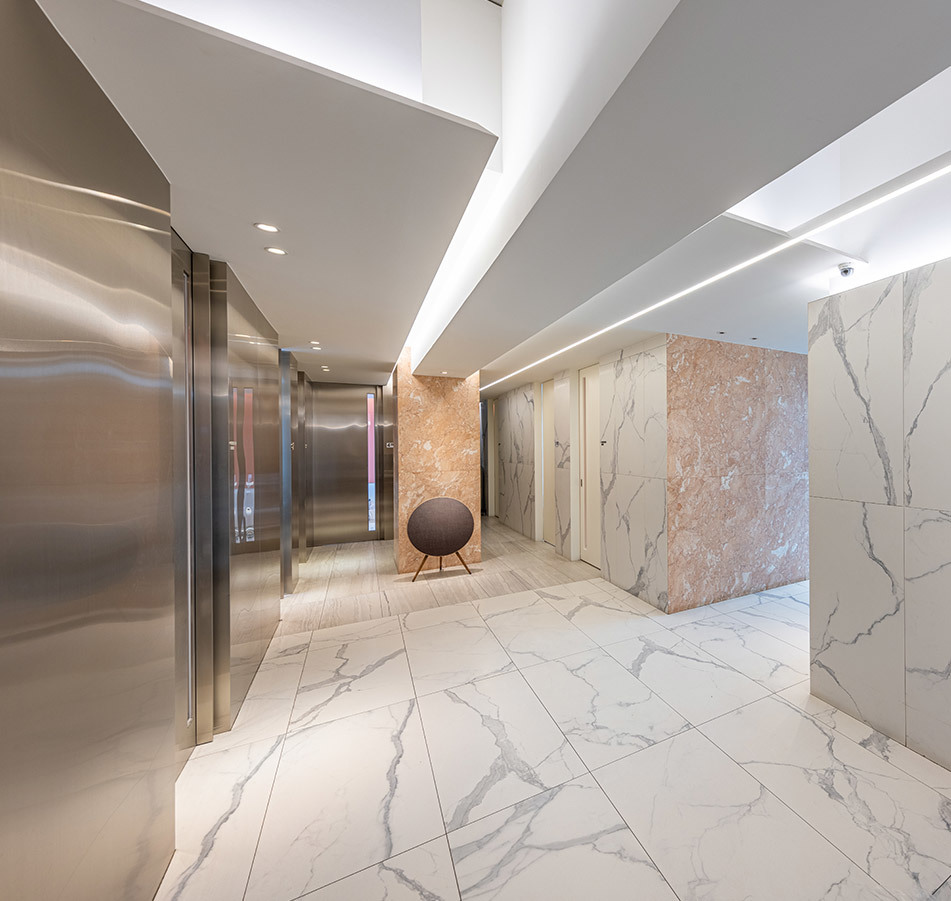 Modern marble lobby interior with elegant lighting and contemporary design elements including a stylish chair and stainless steel elevator doors. • KOREA NEW N DENTAL CLINIC